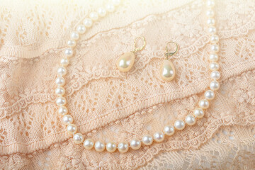 Wedding background. Vintage pearl jewelry earrings and necklace on delicate ivory-colored lace cloth. Elegant gift for woman.