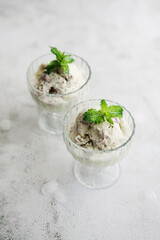 Homemade mint ice cream with mint leaves, pieces of chocolate and ice in glass vases on gray background. Concept of cooking food at home, healthy nutrition.