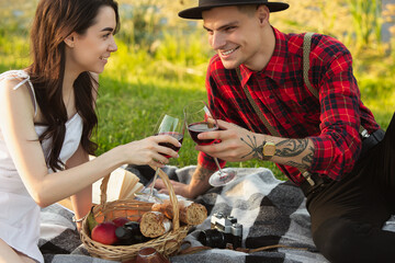 Clinking glasses. Caucasian young, happy couple enjoying weekend together in the park on summer day. Look lovely, happy, cheerful. Concept of love, relationship, wellness, lifestyle. Sincere emotions.