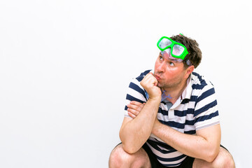 Front view close up squat thinking Man with snorkeling mask for diving stands on white wall