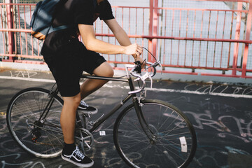 Sportive man in modern headphones listening electronic music ridding on bicycle.Asian male dressed in summer clothes with backpack training on two wheels outdoors in urban setting