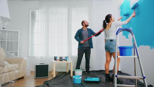 Husband and wife changing wall color using roller brush during home renovation. Home decoration and renovation in cozy apartment flat, repair and makeover
