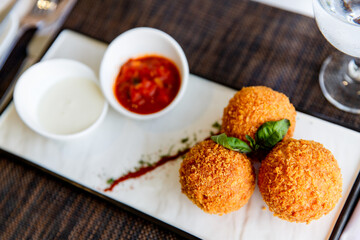 Meatballs in breadcrumbs decorated with mint leaves are served with sauces in a close-up white plate. Healthy food.