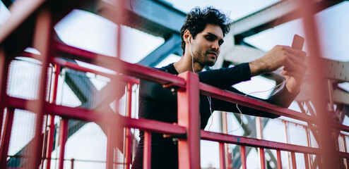 European influence blogger checking statistics of web views for social publication with workout video connected to 4g on mobile device, millennial sportsman messaging with trainer via smartphone