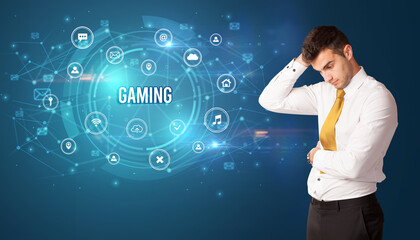 Businessman thinking in front of technology related icons and GAMING inscription, modern technology concept