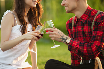 Clinking glasses. Caucasian young couple enjoying weekend together in the park on summer day. Look lovely, happy, cheerful. Concept of love, relationship, wellness, lifestyle. Sincere emotions.