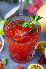 Fresh pink lemonade with raspberries decorated with mint leaves, orange, lime and candied fruit on a decorative background