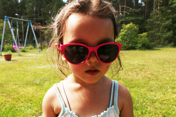 Little girl in beautiful pink sun glasses. A child in the summer in pink sunglasses.