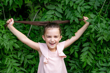 smiling girl 5-6 years old stands in the Park by a tree and holds her hair, happy childhood, child's day