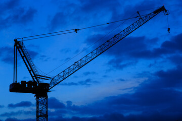 A construction crane silhouetted against a blue evening sky