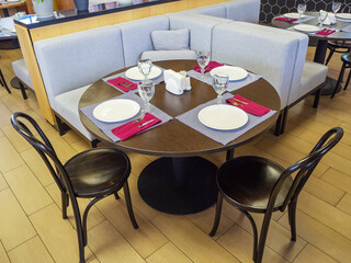 A round wooden table set for four with two wooden chairs stands near a soft corner sofa.