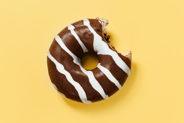 A bitten chocolate donut on a yellow background with a copy space.