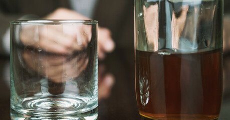 blurry aged person hands on table with transparent glass and blurry cognac bottle