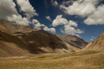 Beautiful view of the mountains and golden grassland under a deep blue sky with clouds and their shadows in the meadow. 