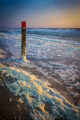 Beach pole during sunset with foam heads on the sand beach on the Dutch Island of Texel beach