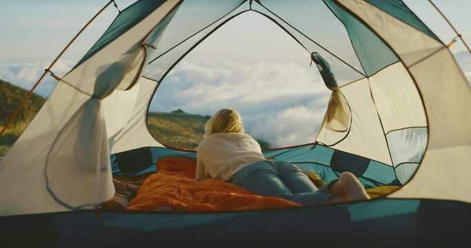 Beautiful woman camping in cozy tent, watching amazing sunset above the clouds, outdoor adventure lifestyle