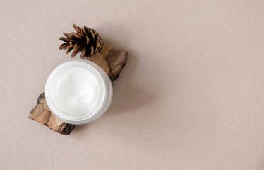 Obraz na płótnie Canvas Moisturizer cream in open glass jar on pine bark and cones on beige flat lay, top view. Natural bio organic eco skincare beauty product