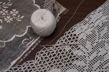 Closeup shot of textile cotton yarn, needle, and filet crochet on a wooden surface