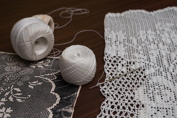 Closeup shot of textile cotton yarn, needle, and filet crochet on a wooden surface