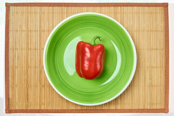 red bell pepper on a green plate on a cane place mat