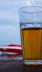 Glass of golden beer on the beach against the background of water and a boat.
