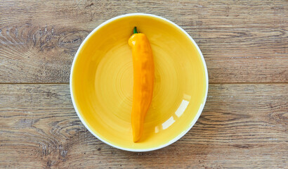 yellow pod of sweet pepper on a yellow plate on a wooden tabletop
