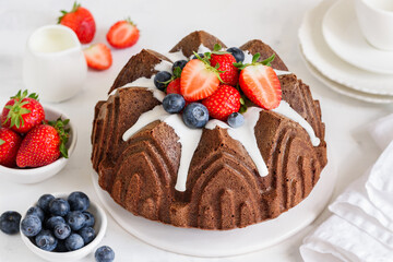 Chocolate bundt cake with cream cheese filling, decorated with fresh strawberries and blueberries. Selective focus.