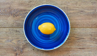 bright yellow lemon on a blue plate on a wooden tabletop