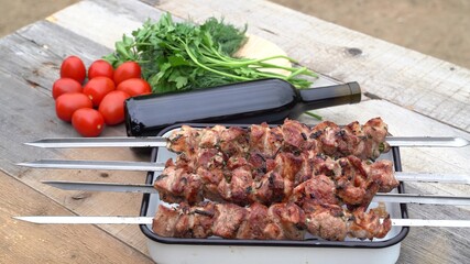 Pork skewers cooked on grill, wine, tomatoes and herbs, in the garden of country house.