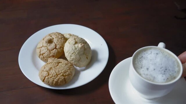 Woman hands puts cup of coffee next to the cookie on the white plate standing on the dark wooden table. Biscuits on the table. Prores 422. High quality FullHD footage. 