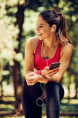Young attractive caucasian female runner taking a break after running and using smart phone.