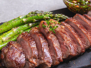 juicy, grilled, sliced beef steak, with roasted asparagus, close up, sauce