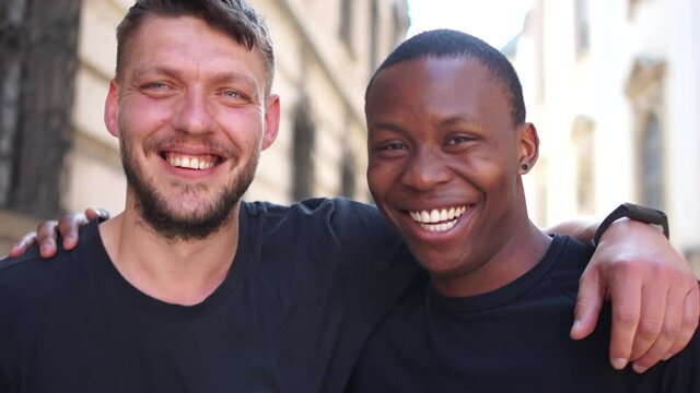 Black man and white man hugging and smiling. Equality, friendship complicity concept. Outdor close portrait of young students. No racism