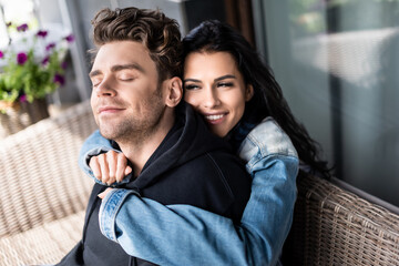Fototapeta premium Beautiful smiling girl hugging handsome boyfriend on wicker sofa on terrace