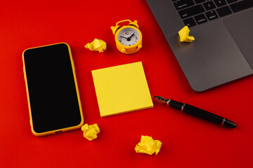 Home office workplace desk concept. Laptop, clock, smarpthone, sticky note and pen on red background.