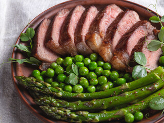 juicy roasted beef sliced steak, with green peas, roasted asparagus, on plate close up