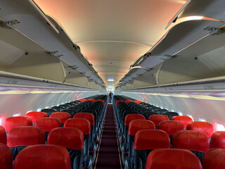 empty aircraft cabin with male cabin crew working in galley. premium and economy seat row in cabin. red seat and black seat.