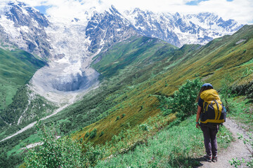 Fototapeta na wymiar Girl traveler with a large backpack in the mountains of Georgia. A complex trekking. View of the Adishi glacier.
