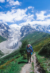 Man traveler with a large backpack in the mountains of Georgia. A complex trekking. View of the Adishi glacier.