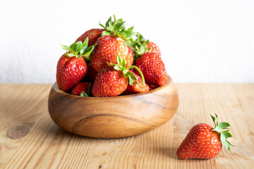 strawberries in a wooden bowl on a wooden table, next to one berry, side view