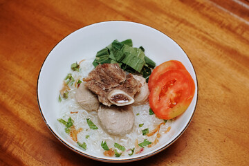 meatball soup with vermicelli and beef ribs. indonesian street food. fresh slices tomatoes. white bowl. pieces of mustard leaf