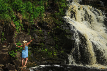 Naklejka na ściany i meble Woman in hat enjoying nature near the forest waterfall.