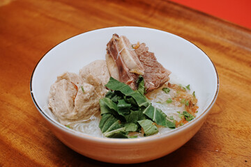 meatball soup with vermicelli and beef ribs. indonesian street food. white bowl. pieces of mustard leaf