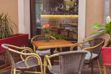 Empty outdoor cafe during quarantine. Restaurant terrace with tables and chairs. Flower on table of street cafe. Elegant street cafe. Outdoor bistro furniture. Cozy patio background.