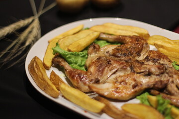Chicken tabaka with fried potatoes and greens on a color background.