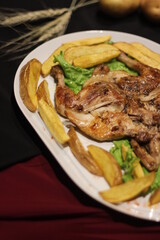 Chicken tabaka with fried potatoes and greens on a color background.