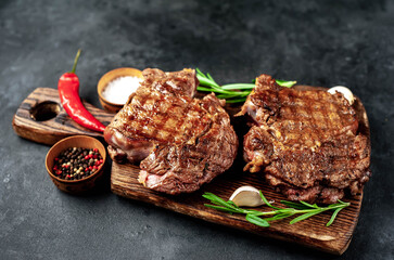 Two grilled beef steaks with spices on a stone background