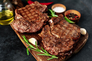 Two grilled beef steaks with spices on a stone background