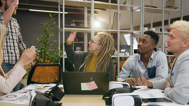 Good-looking positive creative diverse group of friends discussing joint project in office room and greeting his male colleague giving high five