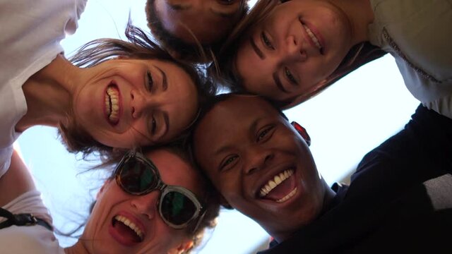 Interracial group of students leaned over the camera against the sky. Close portrait of five young students, tolerance and no racism concept